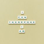 Inspirational phrase 'I Can Therefore I Am' arranged using Scrabble tiles on a green background.